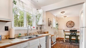 Una cocina con encimera de madera, armarios blancos, un lavamanos y una zona de comedor con mesa y sillas.