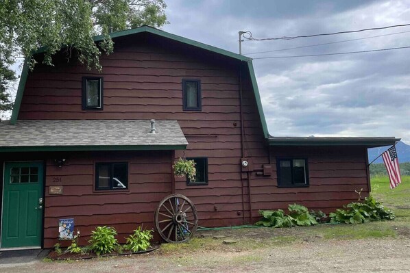 A rustic wooden building with a green door, numbered 251, and a large wheel nearby.