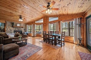 A wooden interior with a fireplace, dining area, and large windows.