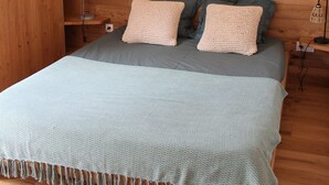 Une chambre avec un mur en bois, un lit recouvert d’une couverture bleue, deux oreillers, un luminaire suspendu et une table de chevet avec une lampe.