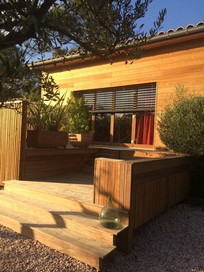 Eine Holzterrasse mit einer Bank, einer Glasflasche und einem Blumentopf.
