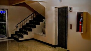 A staircase leading to a second floor, a door with a red object inside, and a small shelf with a white object.