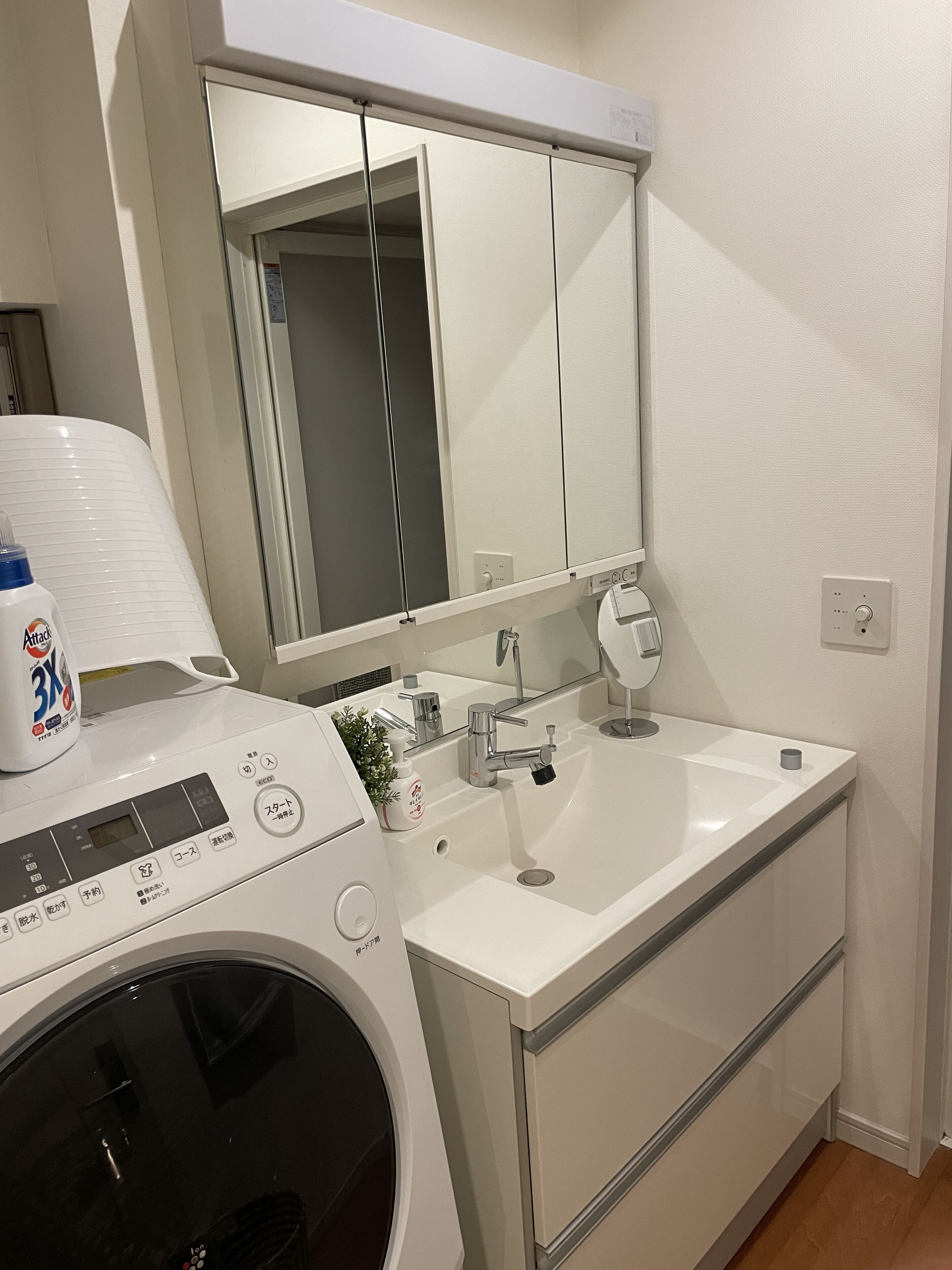 A compact bathroom with a washing machine, a sink, and a mirror.