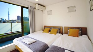 A hotel room with a large bed, two pillows, a window with a view of a cityscape, and an air conditioning unit. - Skytree House In Tokyo (Tokyo)