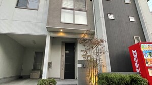 A multi-story residential building with a flat facade, a front entrance with steps, and a small garden area with shrubs. - Skytree House In Tokyo (Tokyo)