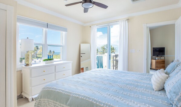 Un dormitorio con una cama grande, un aparador, un televisor y vistas al océano a través de la ventana.