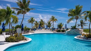 Une piscine d’un bleu éclatant, entourée de palmiers et de chaises longues, avec l’océan en toile de fond.