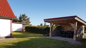 Un espacio de estar al aire libre cubierto con muros de piedra y techo rojo, junto a un edificio con tejado de tejas rojas.