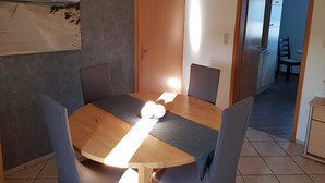 Un comedor con una mesa y sillas de madera, un cuadro en la pared y una puerta que da a otra habitación.