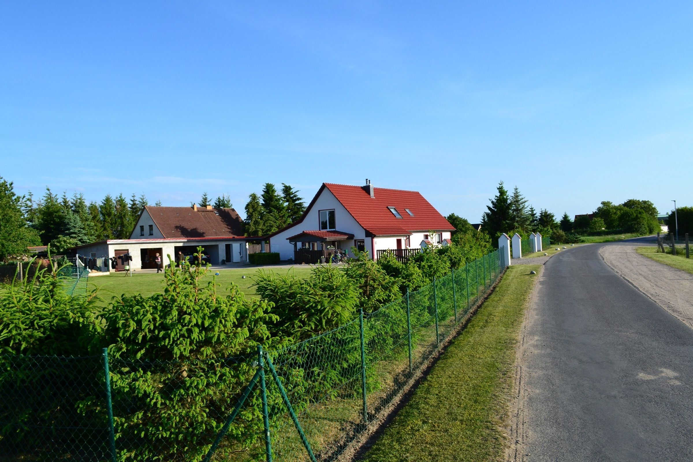 Uma estrada rural ladeada por casas, cercada por vegetação e uma vedação.