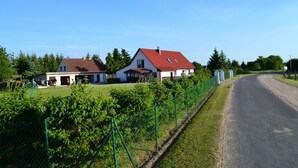 Un camino rural flanqueado por casas, rodeado de follaje y una cerca.