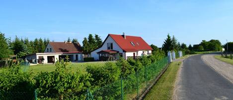 A rural road with houses on either side, surrounded by greenery and a fence.