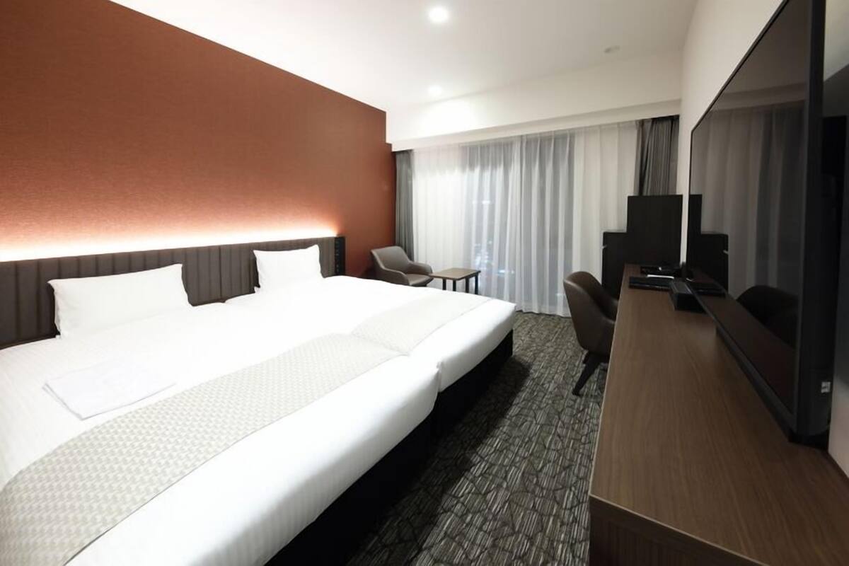 Une chambre d’hôtel avec un grand lit, un bureau, une chaise, une télévision et une fenêtre avec des rideaux.