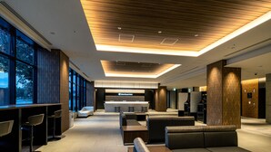 Een moderne hotel lobby met een receptiebalie, zithoek en grote ramen.