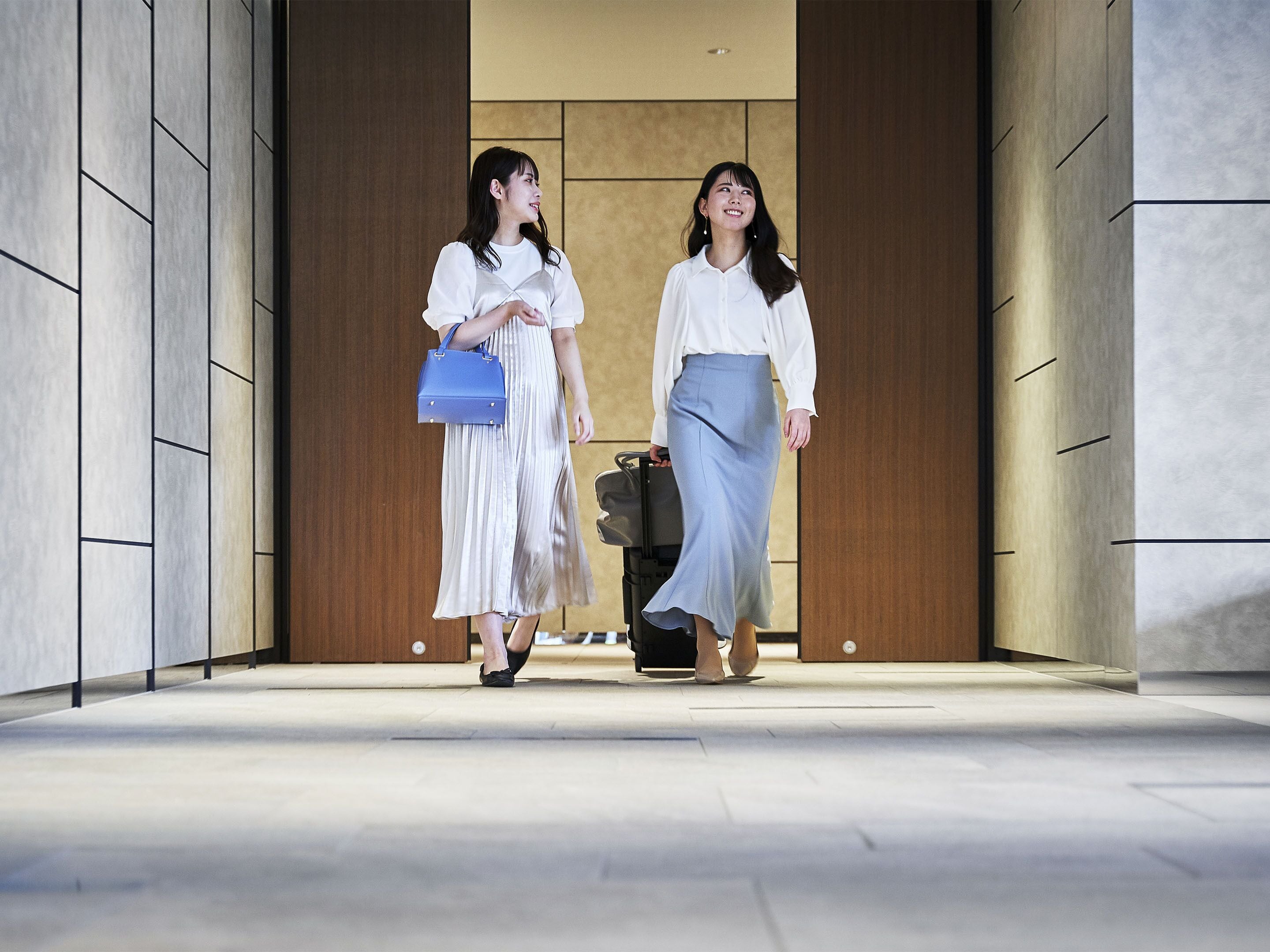 Two individuals walking through a hallway with a modern design, featuring a combination of wood and stone elements.