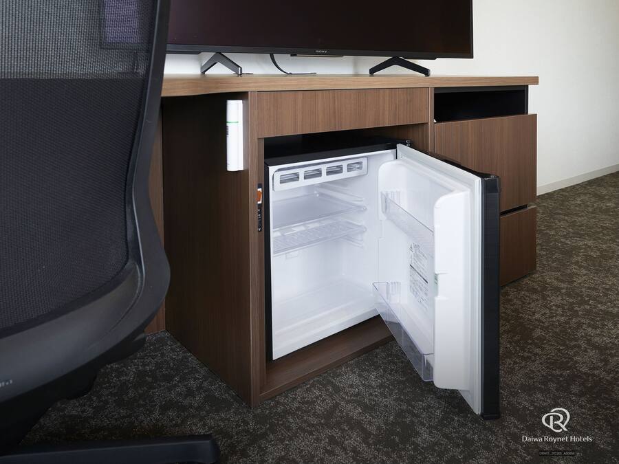 Een kleine kantoorruimte met een ingebouwde koelkast, een flatscreen televisie en een houten bureau.