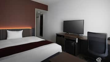 A modern hotel room with a bed, a desk with a flat-screen TV, a chair, and a minibar.