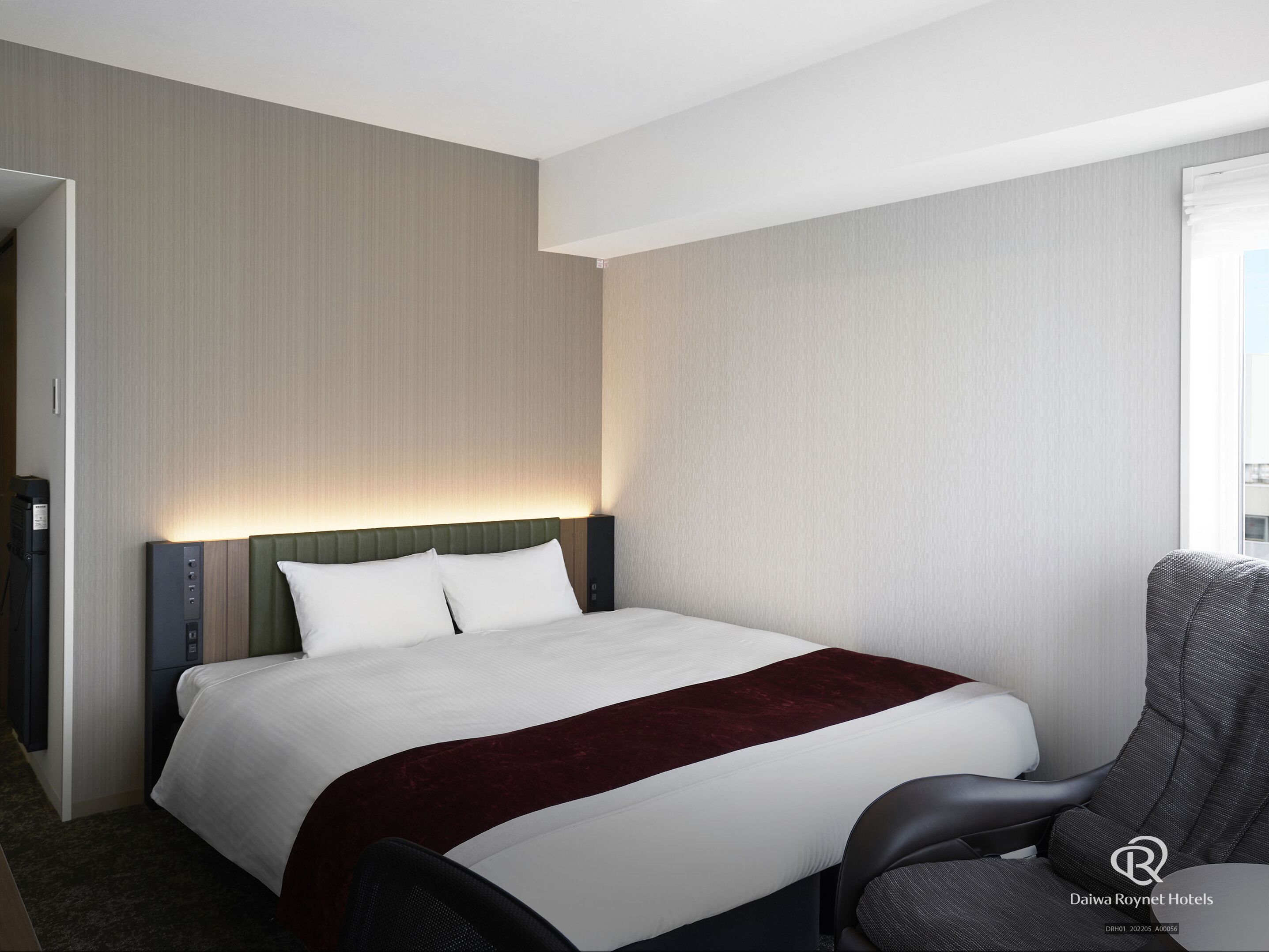 Una habitación de hotel con una cama, una silla y un panel de control en la pared.
