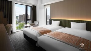 Een hotelkamer met twee bedden, een bureau, een stoel en een groot raam met uitzicht op de stad.
