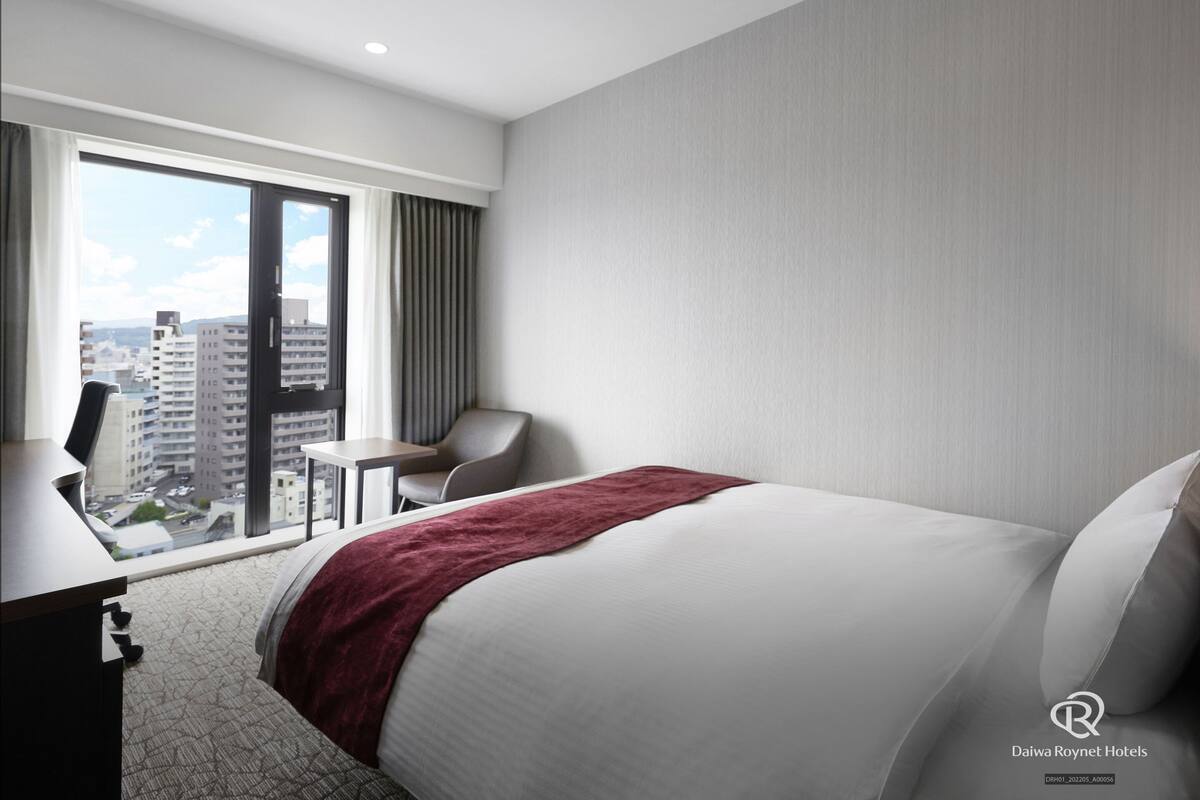 Une chambre d’hôtel avec un grand lit, un bureau, une chaise et une vue sur la ville grâce à une grande fenêtre.