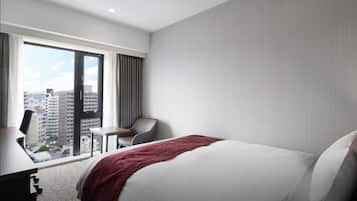 A hotel room with a large bed, a desk, a chair, and a view of the city through a large window.