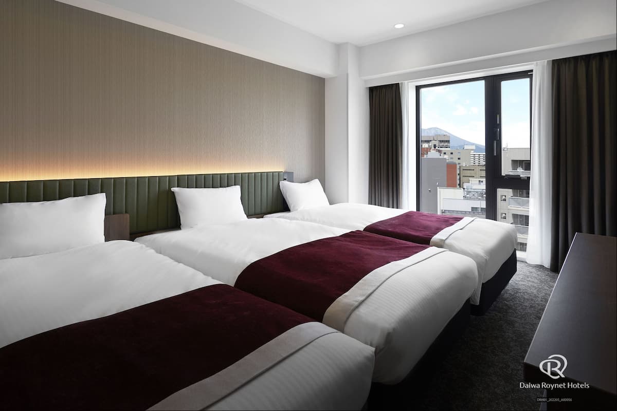 Une chambre d’hôtel avec trois lits, une grande fenêtre donnant sur la ville et un design moderne.