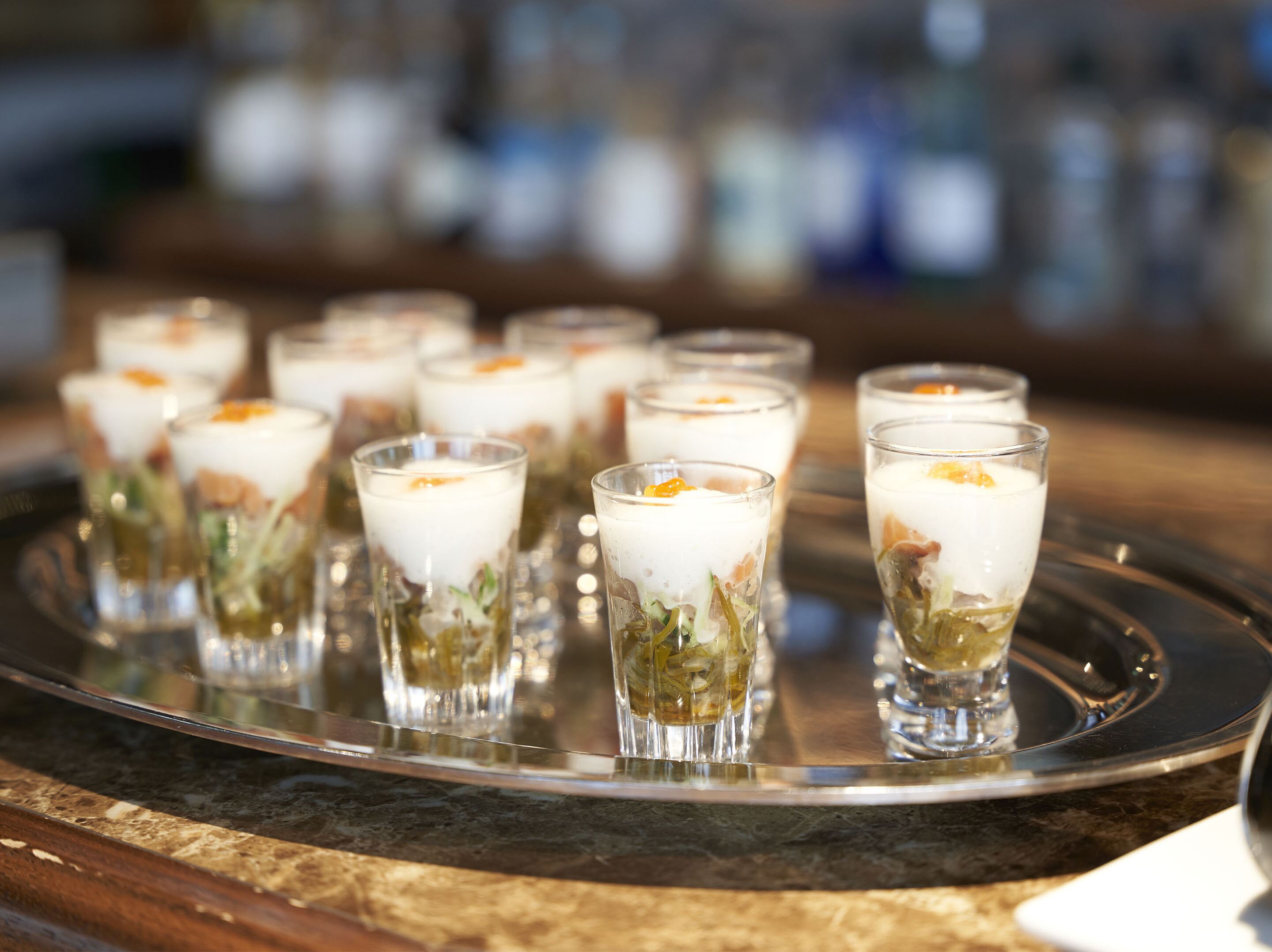 A tray with several glasses of a layered beverage, possibly a cocktail or dessert, with garnishes.