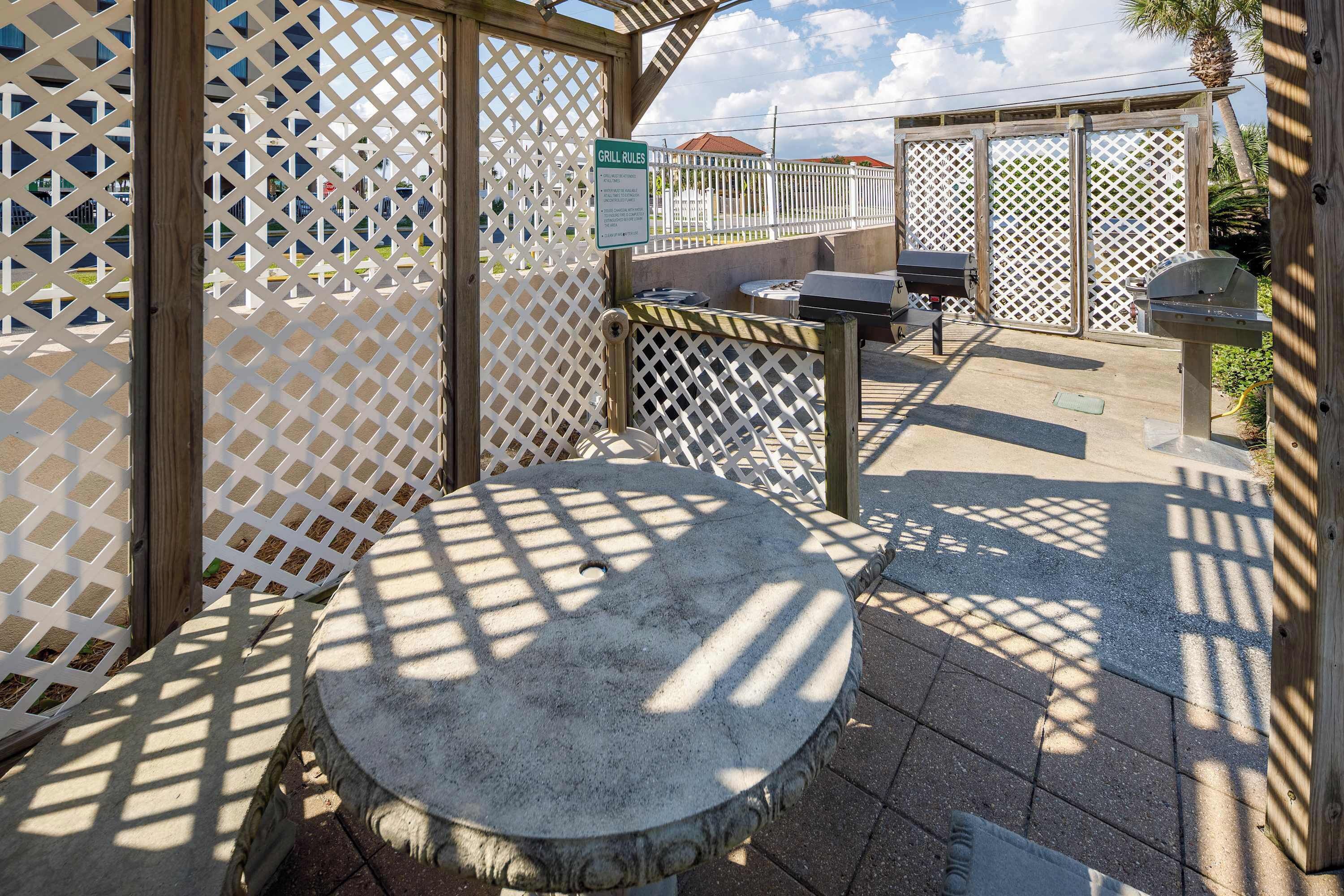 A patio area with a round stone table, a grill, and a wooden fence.