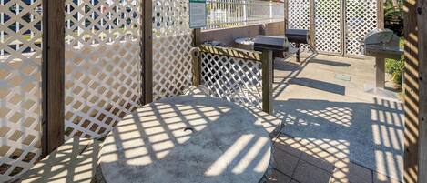 A patio area with a round stone table, a grill, and a wooden fence.
