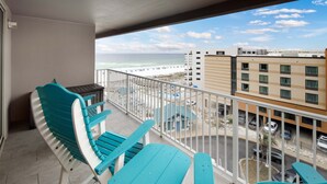A balcony with turquoise chairs and a table, overlooking a beach and a parking area with cars. - Island Princess 719🌊Gulf Views🏖️Free Beach Setup (Fort Walton Beach)