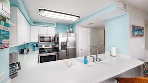 A modern kitchen with white cabinets, stainless steel appliances, a large island with a sink, and a coffee machine. - Island Princess 719🌊Gulf Views🏖️Free Beach Setup (Fort Walton Beach)