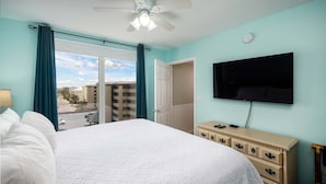 A hotel room with a large bed, a dresser, a TV, and a view of the city through a sliding door. - Island Princess 719🌊Gulf Views🏖️Free Beach Setup (Fort Walton Beach)