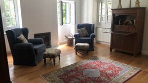 A spacious living room with a fireplace, two armchairs, a matching ottoman, a large patterned rug, and a cabinet with decorative items. - The Garden of Paradise (Santa Cruz)