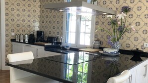 A modern kitchen with a black countertop, white bar stools, and patterned wallpaper. - The Garden of Paradise (Santa Cruz)