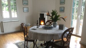 A dining room with a round table, chairs, a fireplace, and framed pictures on the walls. - The Garden of Paradise (Santa Cruz)