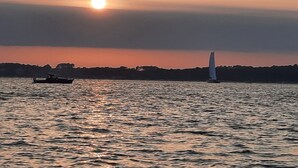 Auringonlasku tyynen vesistön yllä, näkyvissä purjevene ja moottorivene.