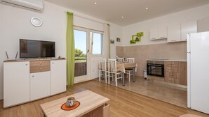 Eine moderne Küche mit weißen Schränken, einem Essbereich mit Tisch und Stühlen, einem Fernseher und einer Klimaanlage.