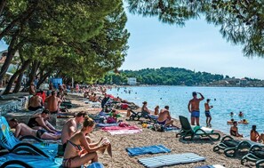 A crowded beach with people sunbathing and swimming, surrounded by trees and a clear view of the water. - Gorgeous apartment in Makarska with WiFi (Makarska)