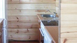 Una cocina compacta con paredes de madera, un lavamanos de acero inoxidable y un lavavajillas.