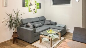 A modern living room with a grey sectional sofa, a glass coffee table, and a potted plant.