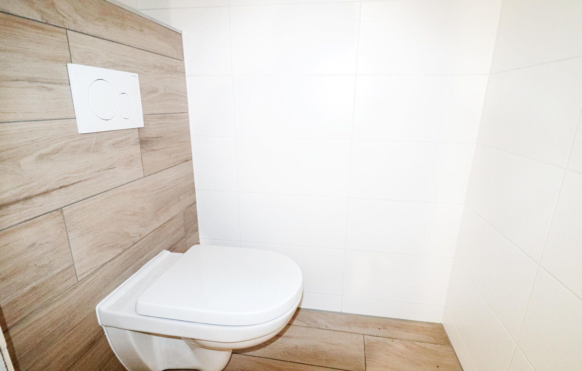 A small, modern bathroom with a white toilet, wooden wall paneling, and white tiled walls.