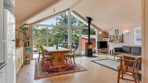Un amplio salón con una gran mesa de madera, sillas, un sofá y un televisor. Hay una chimenea y una estantería llena de libros.