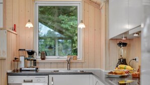 Una cocina moderna con armarios de madera, lavavajillas integrado, ventana con vista a zonas verdes y una licuadora sobre la encimera.