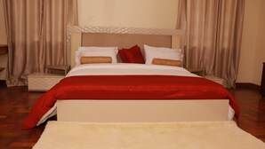Ein ordentlich bezogenes Bett mit weißer und roter Bettwäsche, ein Holzboden und beigefarbene Vorhänge.