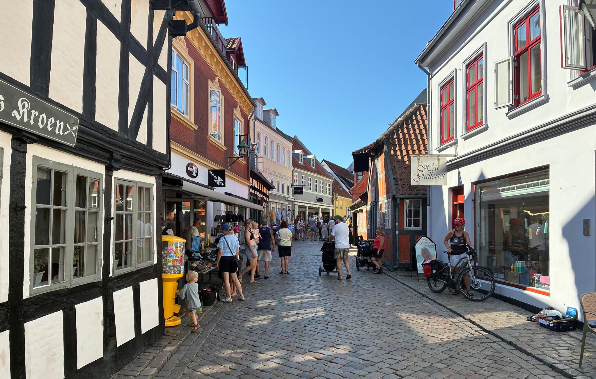 Une rue pavée bordée de bâtiments traditionnels à colombages, de diverses boutiques et d’un flot de piétons.