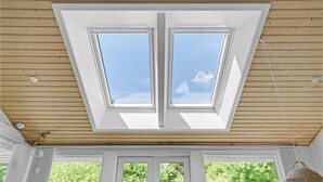 Une pièce dotée d’une lucarne, d’un plafond en bois et offrant une vue sur la verdure environnante.