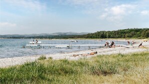 Une plage avec un quai, des zones herbeuses et une forêt en arrière-plan.