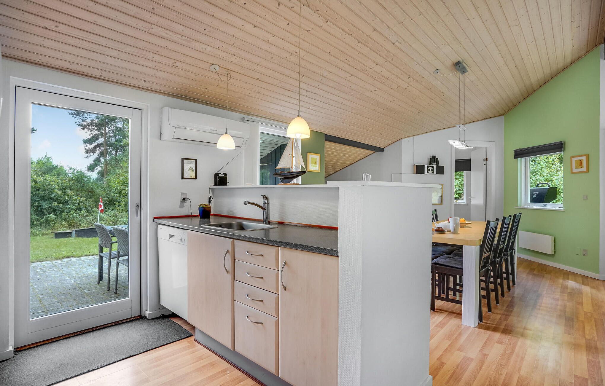 A modern kitchen with a large island, wooden ceiling, and a dining area with a table and chairs.