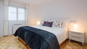 Een slaapkamer met een bed, twee nachtkastjes, een raam met gordijnen en een radiator.