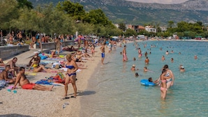 Une plage bondée où les gens se prélassent au soleil et se baignent dans une eau cristalline.